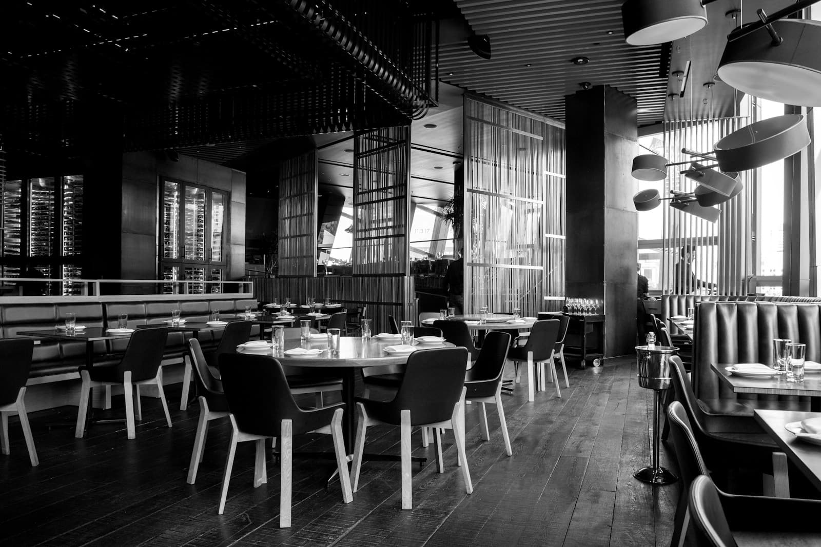 Black and white photograph of a night street dining scene, tables outside a cafe under ambient light